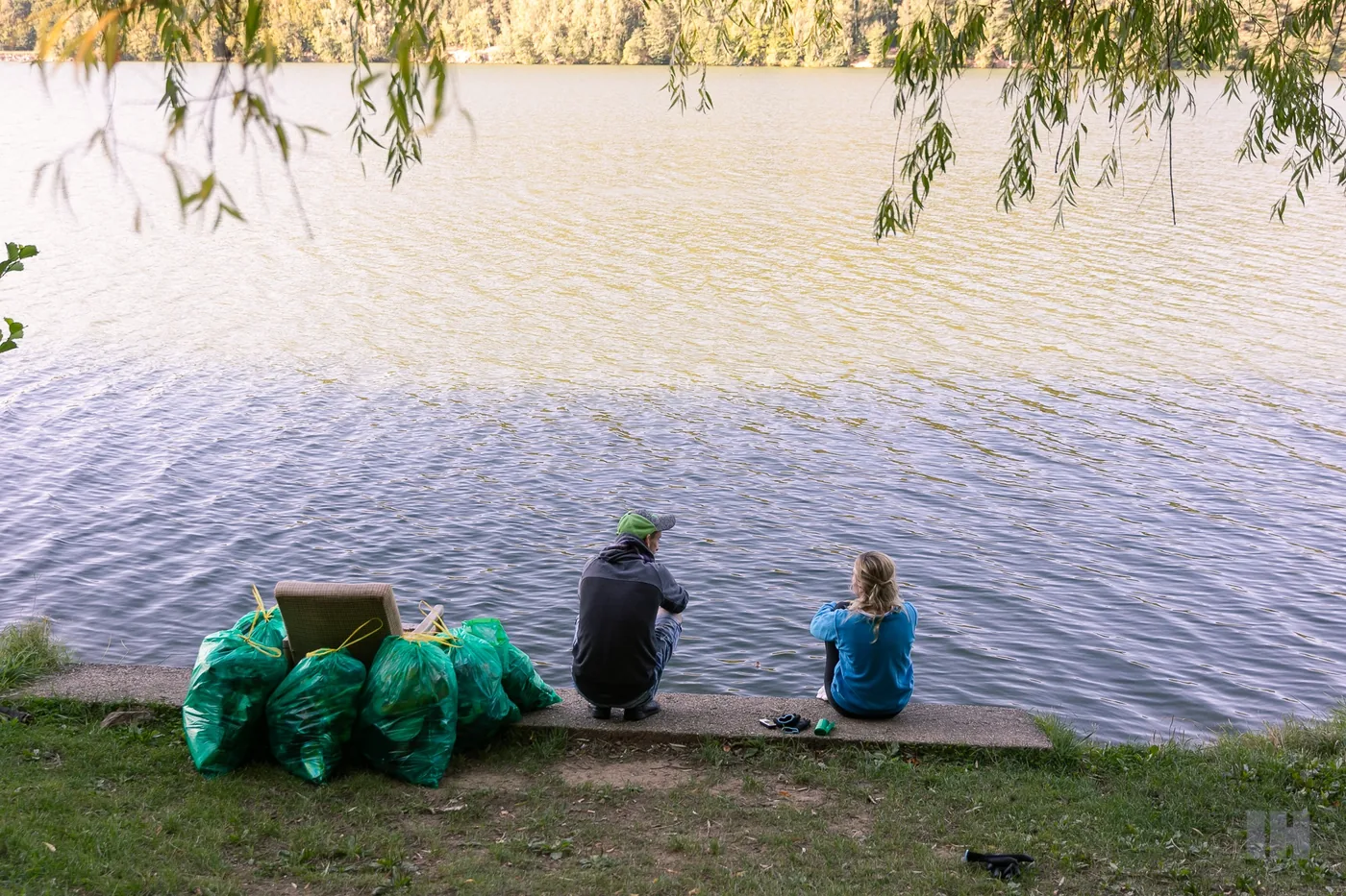 Dobrovoľníci Trash Heroes po zbierke pri vode — zelené vrecia s odpadom